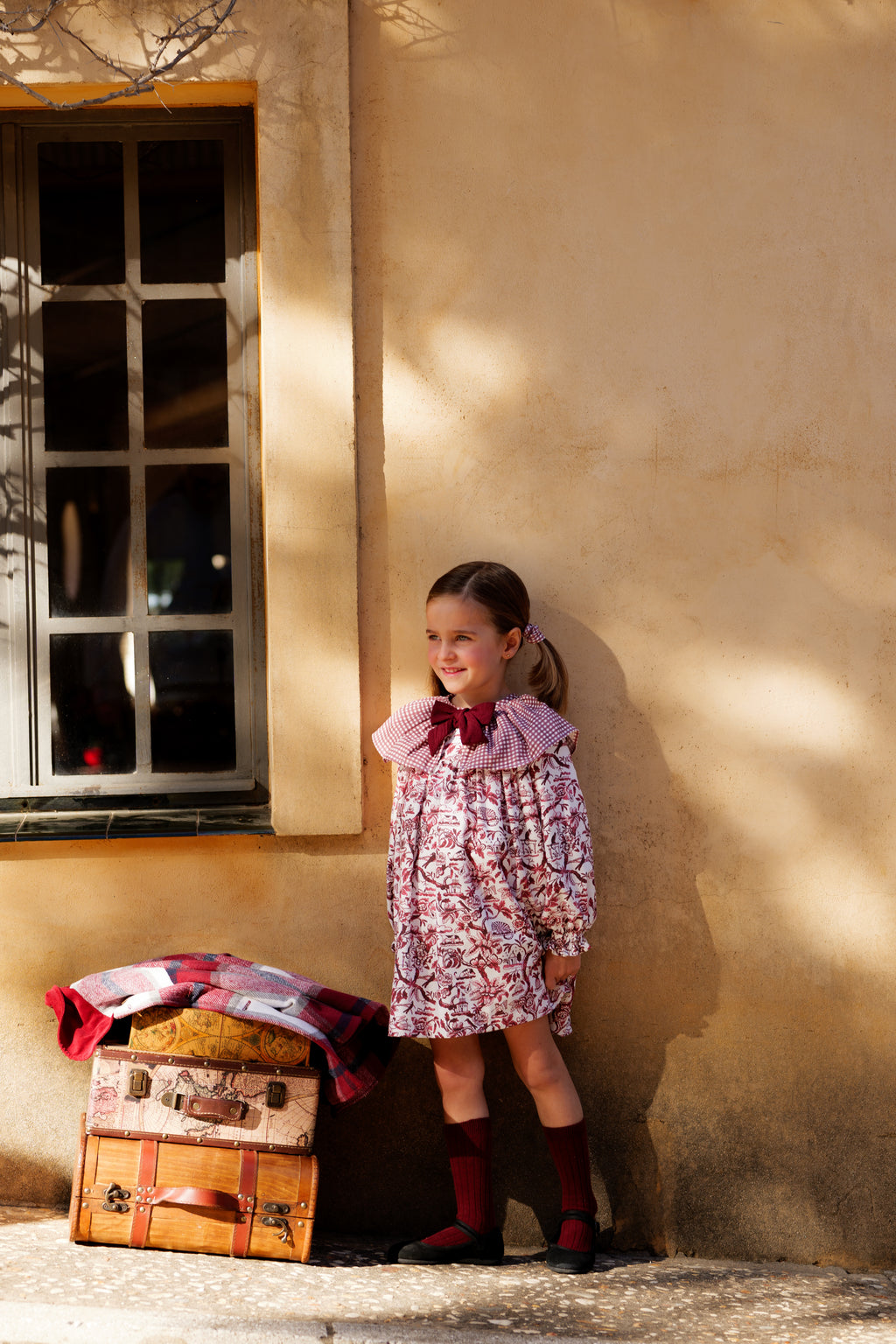 Vestido flores burdeos para niña con vuelo y volante, foto exterior junto a ventana Charanga