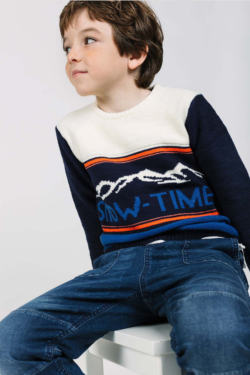 Niño sentado con jersey azul SNOW-TIME estampado montañas estilo invierno foto lifestyle Charanga